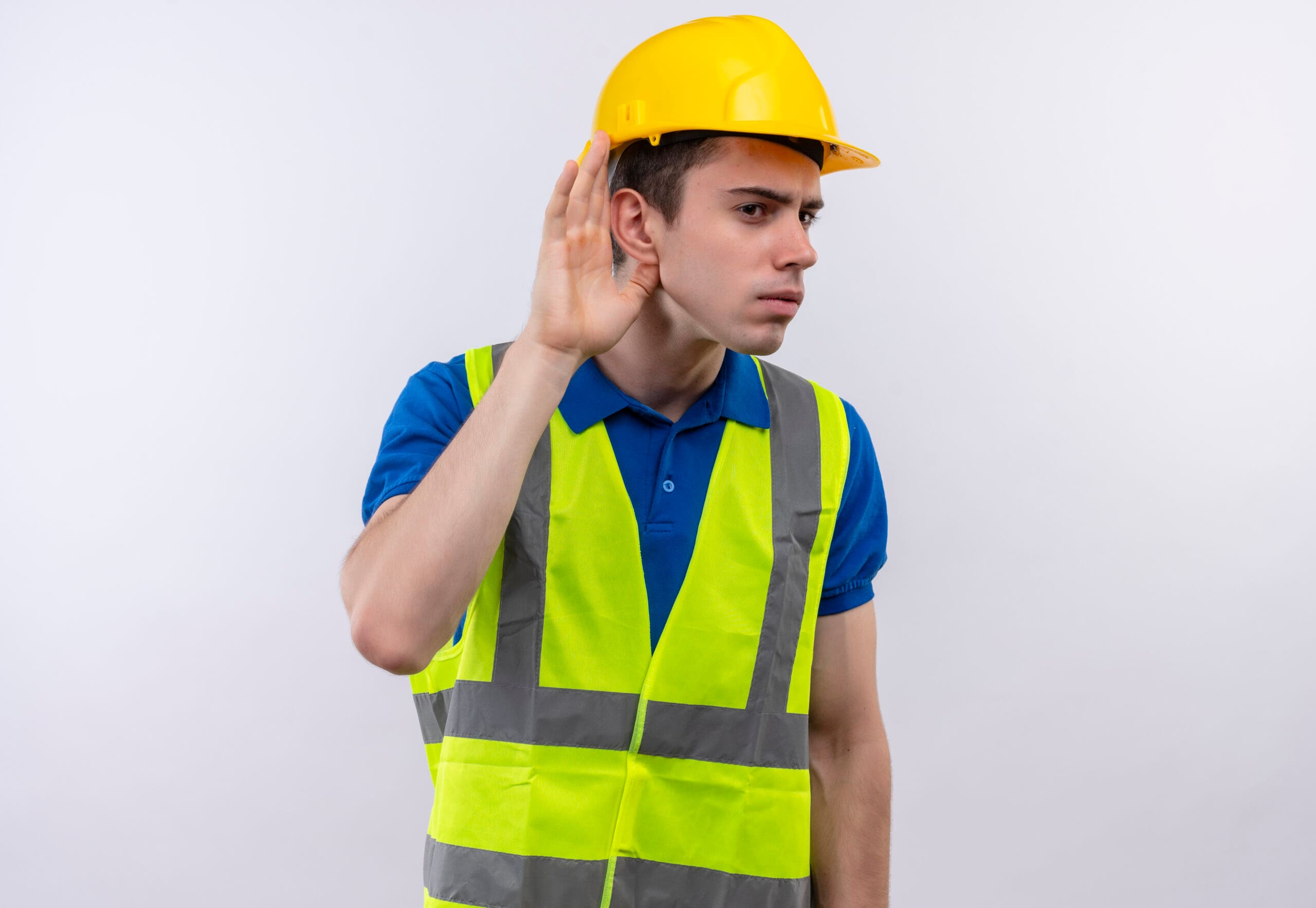 Un joven constructor con uniforme de construcción y casco de seguridad intenta escuchar sobre un fondo blanco aislado